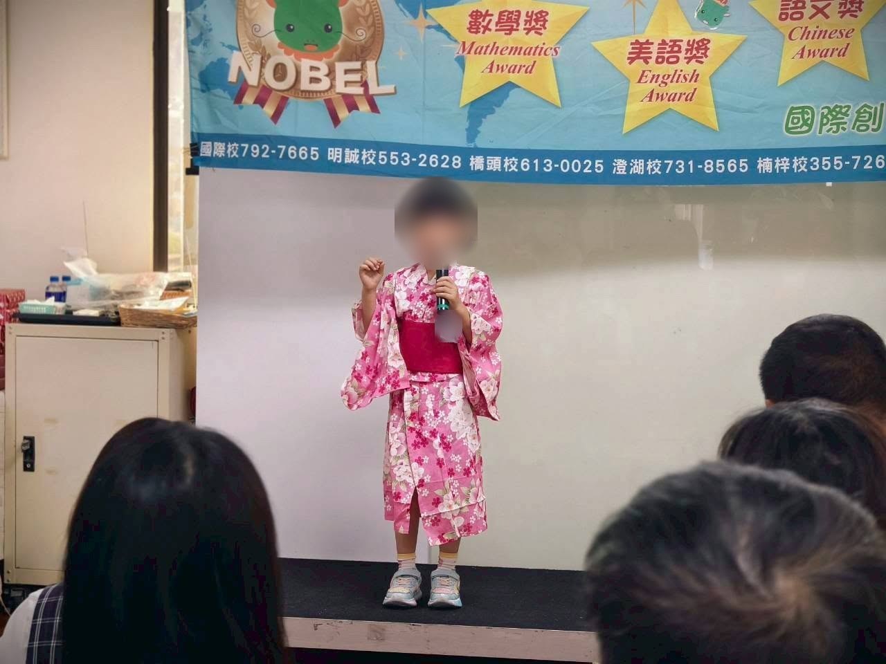高雄雙語幼兒園 諾貝爾明誠 諾貝爾獎活動，孩子拿著麥克風上台，背板寫著數學獎、美語獎、語文獎